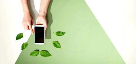 Person holding smartphone with green leavesの写真素材