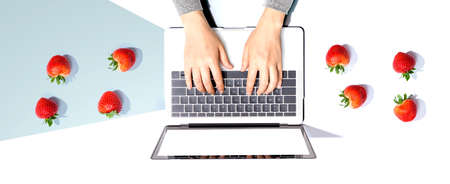 Woman using a laptop computer with fresh strawberriesの写真素材