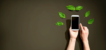 Person holding smartphone with green leavesの写真素材