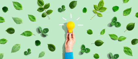 Person holding a lightbulb with green leavesの写真素材
