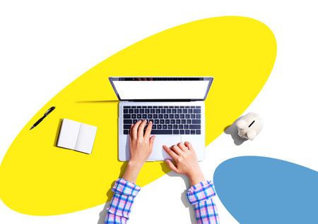 Woman using a laptop computer with a piggy bankの写真素材