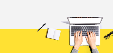 Person using a laptop computer with a notebook and eyeglassesの写真素材