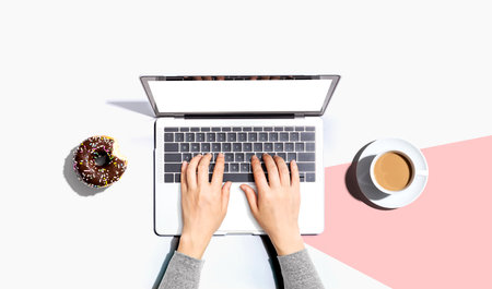Person using a laptop computer with a donut and a cup of coffeeの写真素材