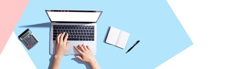 Person using a laptop computer with a notebookの写真素材