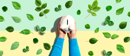 Person holding a piggy bank with green leavesの写真素材