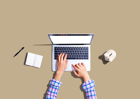 Woman using a laptop computer with a piggy bankの写真素材
