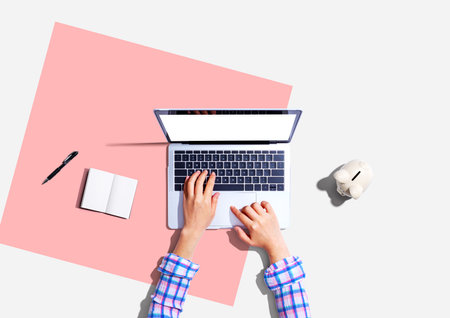 Woman using a laptop computer with a piggy bankの写真素材