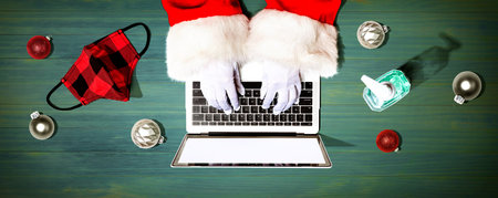 Santa Claus using a laptop computer with a mask and a sanitizer bottleの写真素材