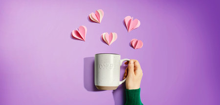 Female hand holding a mug with paper craft heartsの写真素材