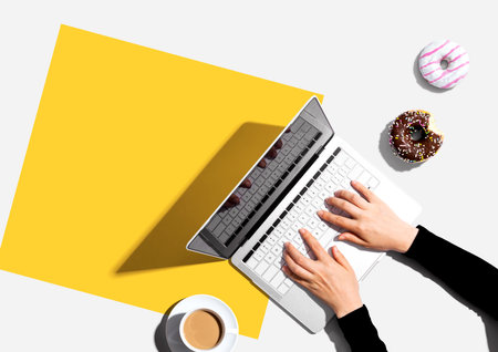Person using a laptop computer with a donut and a cup of coffeeの写真素材