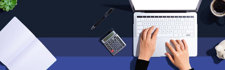 Woman using a laptop computer with a calculatorの写真素材