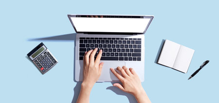 Person using a laptop computer with a notebook and a calculatorの写真素材