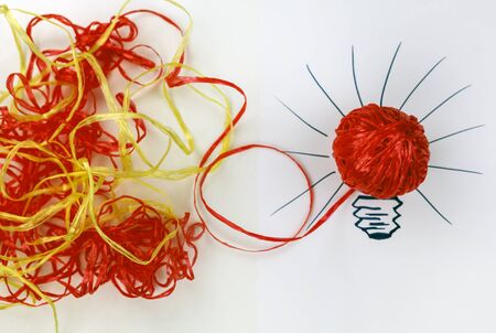 Concept of the idea. From an intricate situation, there is always a way out, entangled ropes of red and yellow, a tangle of rope, placed in a painted light bulbの写真素材
