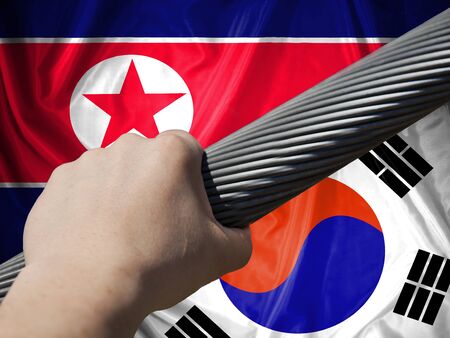 The concept of applying the two countries: North  Korea and South Korea. Flag of  North  Korea, with the flag of South Korea, man's hand compresses stranded steel rope.の写真素材