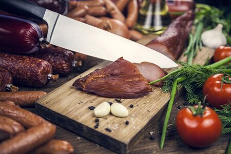 Meat. Sausages, slicing carpaccio, on a wooden table knife cut meat, tomato with dill, parsley and green onionsの写真素材