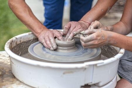 pottery training, a close-up of a man potter teaches a woman how to properly mold a bowl of brown clay on a potterの写真素材