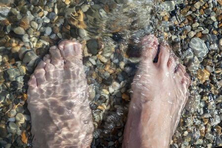 Foots girl on the stones of the sea beach in the incident wave.の写真素材