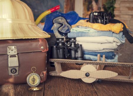 Travel concept background. Overhead view of Traveler's accessories, Essential vacation items, old suitcase, compass, straw hat, on a wooden background, in the background the contour of the map of the continents of the worldの写真素材