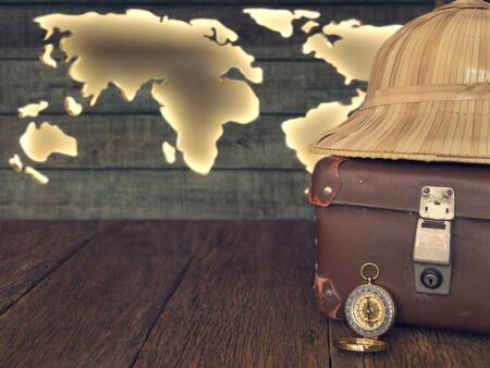 Travel concept background. Old suitcase, compass, straw hat, on a wooden background, in the background the contour of the map of the continents of the world, copy space, tonedの写真素材