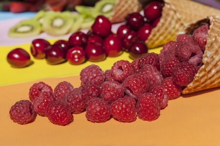 Scattered fruits (strawberries, pineapple, raspberries, kiwi, blackberries, cherries) in waffle, cone cups on a bright colored backgroundの写真素材