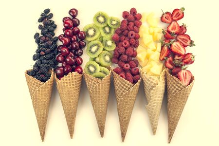 Scattered fruits (strawberries, pineapple, raspberries, kiwi, blackberries, cherries) in waffle, cone cups on  a whait background; tonedの写真素材