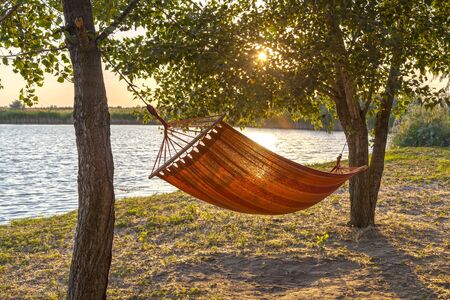 The concept of a picnic, solitude with nature and relaxation, a hammock against the backdrop of a lake in the rays of the setting sunの写真素材