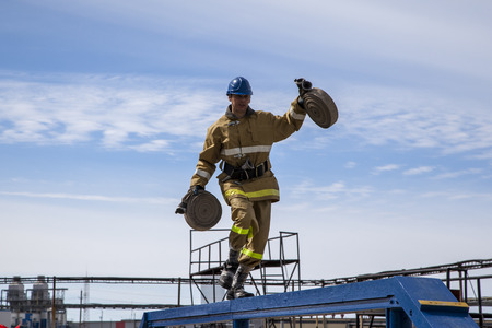 Nadym, Russia - april 27, 2017: A professional fireman in a special suit jumps over a barrier .Regional fire-fighting in the training area with urban and contract firefighters.のeditorial素材