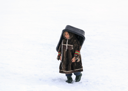 Nadym, Russia - april 27, 2018:tundra, open area, children ride on sledges, children of Nenets in national clothesのeditorial素材