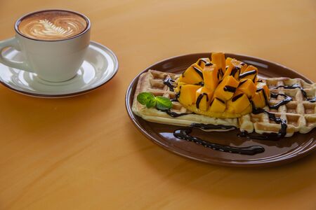 Viennese waffles with ice cream and slices of mango doused with chocolate, on an orange backgroundの写真素材