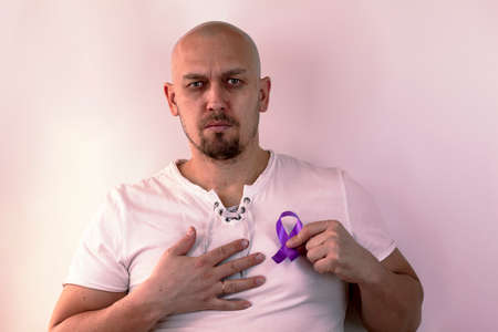 Medicine, cancer, young handsome bald man holding a cancer violet ribbon, standing with a confident expression on his face, holding his chest with his hand, tonedのeditorial素材