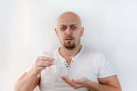Feeling sick concept. Daily norm of vitamins, effective drugs, modern pharmacy for body and mental health concept . Man with glass of water, takes pillsのeditorial素材