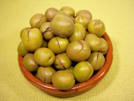 Bunch of green olives on a clay plate, on a yellow cloth on a white background.の写真素材