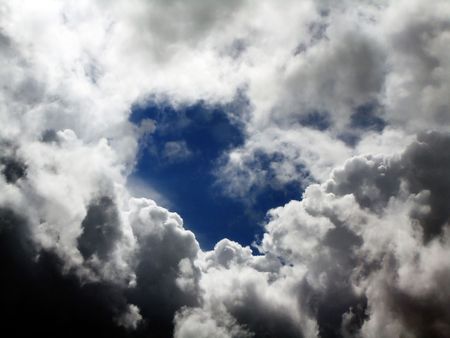 overcast sky with a misc of heavy dark and white clouds, revealing at the center a blue sky.の写真素材