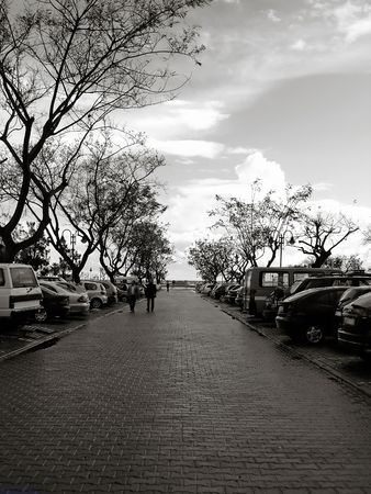 Parking lot with cars, trees and people passing by.の写真素材