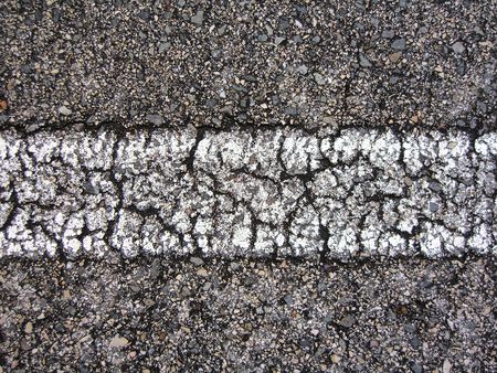 Straight white line view of an asphalt road with many cracks.の写真素材