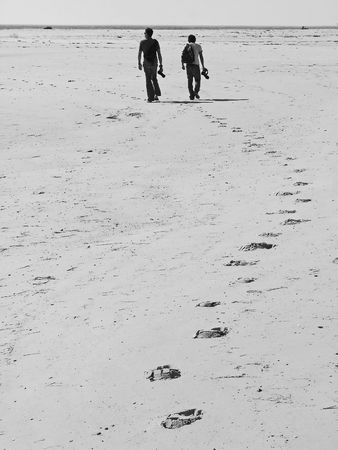 Two male photographers with their cameras walking down the beach.の写真素材