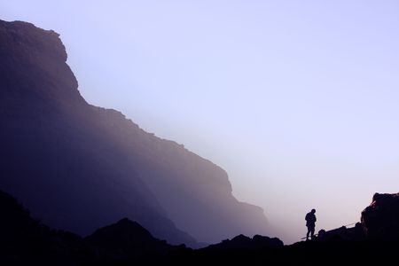 Fisherman on the lower right side being bathed with morning fog over the rocky shore.