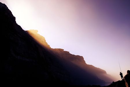 Fisherman on the lower right side being bathed with morning ray lights through the mystical fog over the rocky shore.の写真素材