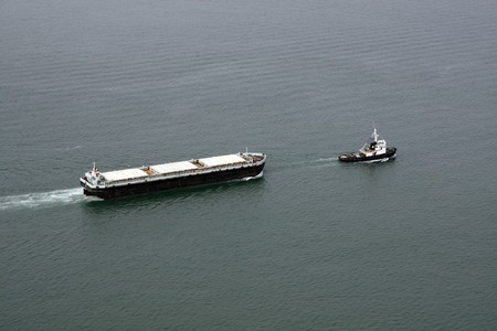 Aerial view of a cargo transportation ship escorted by a small fishing boat.