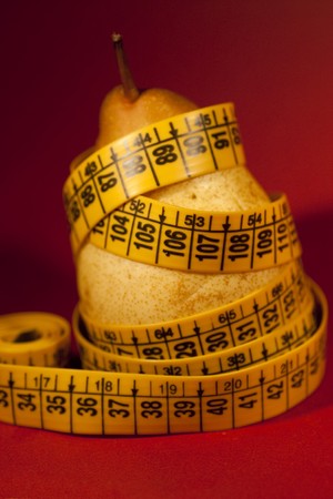Close view of a pear with measuring tape over a red background.の写真素材