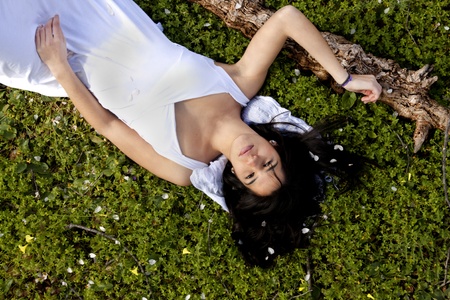 View of a beautiful girl on a white dress on a green grass field next to a almond treeの写真素材