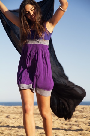 View of a beautiful young girl playful with a purple dress in the beach.の写真素材