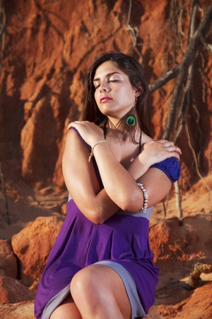 View of a beautiful young girl with a purple dress standing on a red cliff on the beach.の写真素材