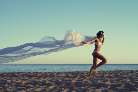View of a beautiful young girl with a white bikini running on the beach.の写真素材