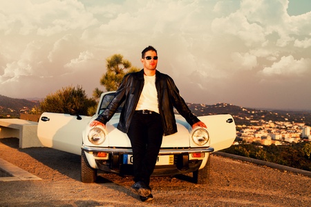 View of a young male with a jacket next to his white convertible car.