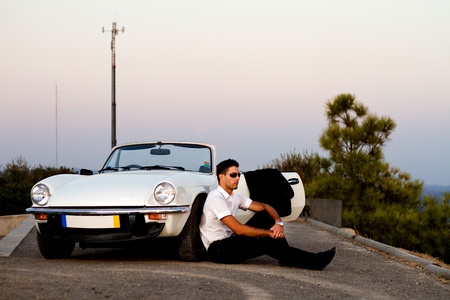 View of a young male with a jacket next to his white convertible car.