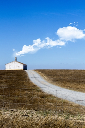 View of a conceptual photo with a lonely house with road on a dry land with white clouds exiting the chimney.の写真素材