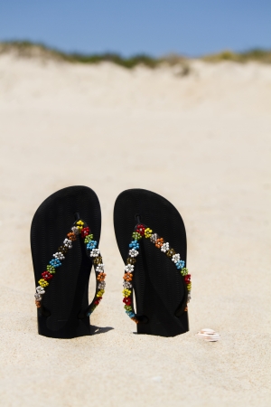 View of two beach sandals with flower detail stuck on the sand.の写真素材