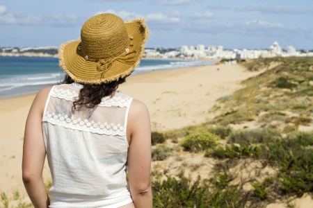 Close view detail of a beautiful young woman with a straw hat in summer clothes, watching a  beautiful beach landscape.の写真素材
