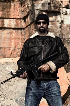 View of a man with a machine gun in jeans and jacket on a stone quarry.の写真素材